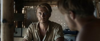 Movie still from “Kon-Tiki” (2012), directed by Espen Sandberg – A man with blonde long hair and a tan shirt looking into a mirror; Close Up shot, Over the shoulder angle