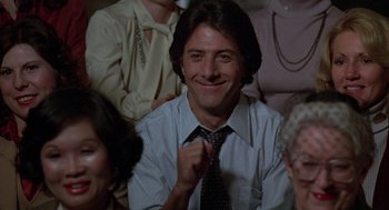 Movie still from “Kramer vs. Kramer” (1979), directed by Robert Benton – A man in a suit and tie smiling for the camera; Close Up shot, Over the shoulder angle