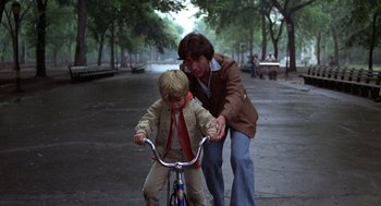 Movie still from “Kramer vs. Kramer” (1979), directed by Robert Benton – A man helping a child on a bicycle; Wide shot, Over the shoulder angle