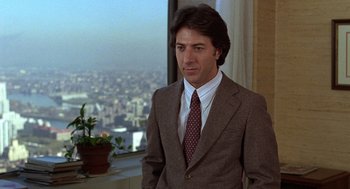 Movie still from “Kramer vs. Kramer” (1979), directed by Robert Benton – A man wearing a suit and tie standing in front of a window; Medium shot, Over the shoulder angle