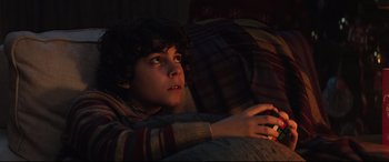 Movie still from “Krampus” (2015), directed by Michael Dougherty – A young boy laying in a bed looking at a phone; Close Up shot, High angle