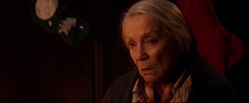 Movie still from “Krampus” (2015), directed by Michael Dougherty – An older woman looking at the camera in a dimly - lit room; Close Up shot, Over the shoulder angle