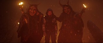 Movie still from “Krampus” (2015), directed by Michael Dougherty – A man standing next to two people wearing masks; Medium shot, High angle