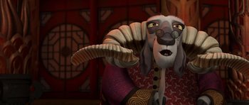 Movie still from “Kung Fu Panda 2” (2011), directed by Jennifer Yuh Nelson – An animated goat sitting on a chair with a red background; Close Up shot, Over the shoulder angle