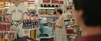 Movie still from “Labor Day” (2013), directed by Jason Reitman – A woman in a plaid dress looking at baby supplies in a store; Wide shot, High angle