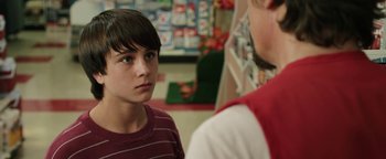Movie still from “Labor Day” (2013), directed by Jason Reitman – A young boy standing in front of a man in a store; Close Up shot, Over the shoulder angle