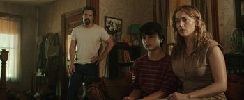 Movie still from “Labor Day” (2013), directed by Jason Reitman – A man standing next to a young boy in a living room; Medium shot, Over the shoulder angle