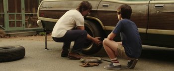 Movie still from “Labor Day” (2013), directed by Jason Reitman – Two men are changing a tire on a car; Medium shot, Over the shoulder angle