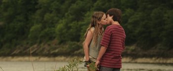 Movie still from “Labor Day” (2013), directed by Jason Reitman – A boy and a girl kissing in front of trees; Medium shot, Low angle