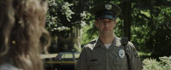 Movie still from “Labor Day” (2013), directed by Jason Reitman – A man in a police uniform standing in front of a yellow car; Medium shot, Over the shoulder angle
