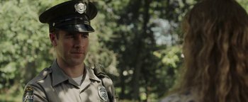 Movie still from “Labor Day” (2013), directed by Jason Reitman – A man in a police uniform standing in front of trees; Close Up shot, Over the shoulder angle