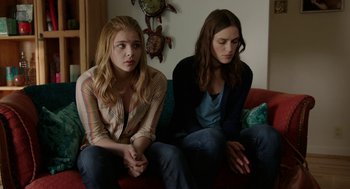 Movie still from “Laggies” (2014), directed by Lynn Shelton – Two young women sitting on a red couch next to each other; Medium shot, Over the shoulder angle