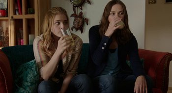 Movie still from “Laggies” (2014), directed by Lynn Shelton – Two young women sitting on a couch drinking juice; Medium shot, Over the shoulder angle