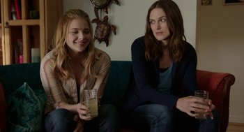 Two women sitting on a couch with a drink in their hands