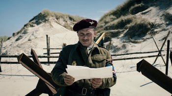 Movie still from “Land of Mine” (2015), directed by Martin Zandvliet – A man in a military uniform is holding a paper; Medium shot, Over the shoulder angle