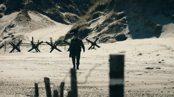 Movie still from “Land of Mine” (2015), directed by Martin Zandvliet – A man walking on the beach with a rifle in his hand; Extreme Wide shot, Low angle