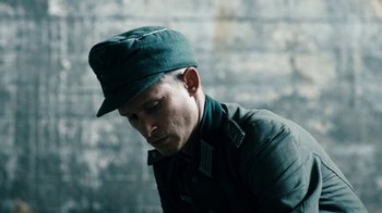 Movie still from “Land of Mine” (2015), directed by Martin Zandvliet – A man wearing a green hat is looking down at the ground; Close Up shot, High angle