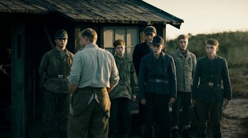 Movie still from “Land of Mine” (2015), directed by Martin Zandvliet – A group of men standing next to each other in front of a building; Medium shot, Over the shoulder angle