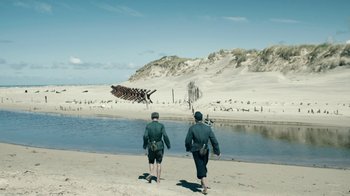 Movie still from “Land of Mine” (2015), directed by Martin Zandvliet – Two men walking on the beach near the water; Extreme Wide shot, High angle