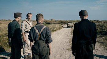 Movie still from “Land of Mine” (2015), directed by Martin Zandvliet – A group of men standing on a dirt road; Medium shot, Over the shoulder angle