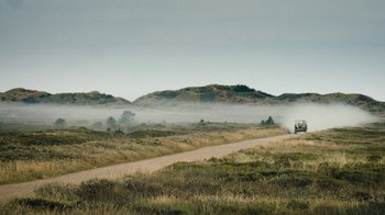 Movie still from “Land of Mine” (2015), directed by Martin Zandvliet – A truck driving down a dirt road near a field; Extreme Wide shot, Low angle