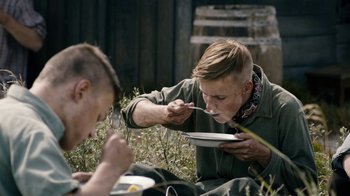 Movie still from “Land of Mine” (2015), directed by Martin Zandvliet – Two men are sitting in the grass and eating food; Medium shot, Over the shoulder angle