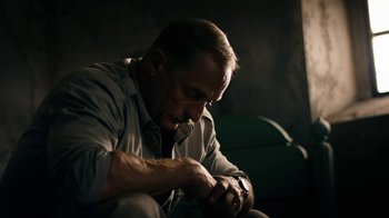 Movie still from “Land of Mine” (2015), directed by Martin Zandvliet – A man looking down at his watch while sitting on a couch; Close Up shot, Low angle