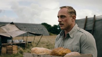 Movie still from “Land of Mine” (2015), directed by Martin Zandvliet – A man standing in a field holding a box of bread; Close Up shot, Over the shoulder angle