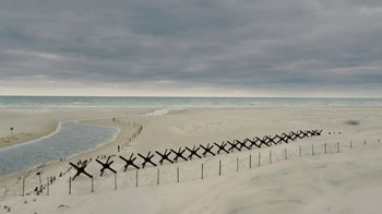 Movie still from “Land of Mine” (2015), directed by Martin Zandvliet – A beach that has a fence on top of it; Extreme Wide shot, High angle