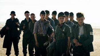 Movie still from “Land of Mine” (2015), directed by Martin Zandvliet – A group of young men standing next to each other on a beach; Medium shot, Low angle