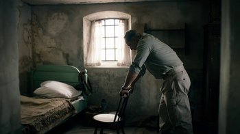 Movie still from “Land of Mine” (2015), directed by Martin Zandvliet – A man is holding a chair in a room with a bed; Medium shot, Low angle