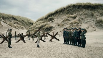 Movie still from “Land of Mine” (2015), directed by Martin Zandvliet – A group of men standing on top of a sandy beach; Extreme Wide shot, High angle