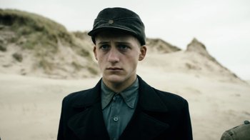 Movie still from “Land of Mine” (2015), directed by Martin Zandvliet – A young man wearing a hat and a jacket; Close Up shot, Low angle