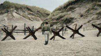 Movie still from “Land of Mine” (2015), directed by Martin Zandvliet – A man walking on the sand near a fence; Extreme Wide shot, High angle