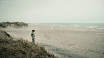 Movie still from “Land of Mine” (2015), directed by Martin Zandvliet – A man standing on top of a hill looking out at the ocean; Extreme Wide shot, High angle