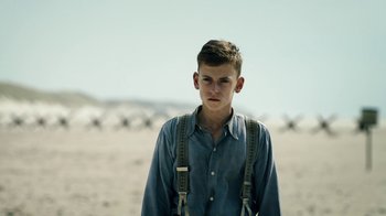 Movie still from “Land of Mine” (2015), directed by Martin Zandvliet – A young man wearing suspenders standing in a field; Medium shot, Low angle