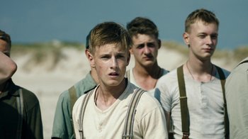 Movie still from “Land of Mine” (2015), directed by Martin Zandvliet – A group of young men standing next to each other on a beach; Close Up shot, Low angle