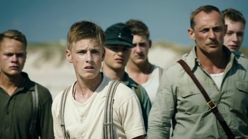 Movie still from “Land of Mine” (2015), directed by Martin Zandvliet – A group of young men standing next to each other on a beach; Medium shot, Low angle