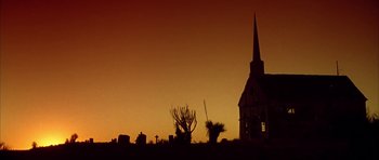 Movie still from “Last Man Standing” (1996), directed by Walter Hill – A church with a steeple at sunset with a cemetery in the background; Extreme Wide shot, Low angle