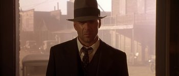 Movie still from “Last Man Standing” (1996), directed by Walter Hill – A man wearing a suit and a hat in front of a building; Close Up shot, Low angle