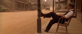 Movie still from “Last Man Standing” (1996), directed by Walter Hill – A man sitting on a chair on the side of the street; Wide shot, Low angle