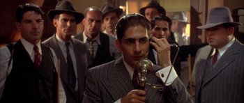Movie still from “Last Man Standing” (1996), directed by Walter Hill – A group of men standing around a man holding a microphone; Medium shot, Low angle