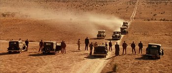 Movie still from “Last Man Standing” (1996), directed by Walter Hill – A group of men standing around a dirt road; Extreme Wide shot, High angle