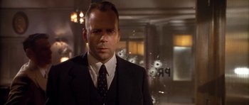 Movie still from “Last Man Standing” (1996), directed by Walter Hill – A man in a suit and tie standing in front of bullet holes in a building; Close Up shot, Low angle