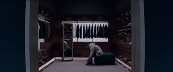 Movie still from “Fifty Shades of Grey” (2015), directed by Sam Taylor-Johnson – A man sitting on top of an ottoman in front of a mirror; Wide shot, High angle