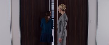 Movie still from “Fifty Shades of Grey” (2015), directed by Sam Taylor-Johnson – Two women in business attire standing in front of a window; Medium shot, Over the shoulder angle