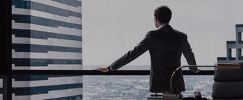 Movie still from “Fifty Shades of Grey” (2015), directed by Sam Taylor-Johnson – A man in a business suit looking out a window; Medium shot, Over the shoulder angle