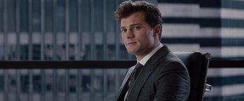 Movie still from “Fifty Shades of Grey” (2015), directed by Sam Taylor-Johnson – A man wearing a suit and tie in front of a building; Close Up shot, Over the shoulder angle