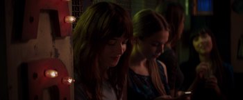 Movie still from “Fifty Shades of Grey” (2015), directed by Sam Taylor-Johnson – Two young women sitting next to each other in a dark room; Close Up shot, Over the shoulder angle