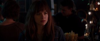 Movie still from “Fifty Shades of Grey” (2015), directed by Sam Taylor-Johnson – A young woman with long hair and bangs looking at the camera; Close Up shot, Over the shoulder angle